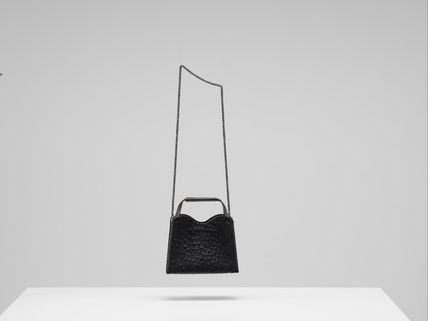 Black handbag with a long strap on a white surface and light gray background