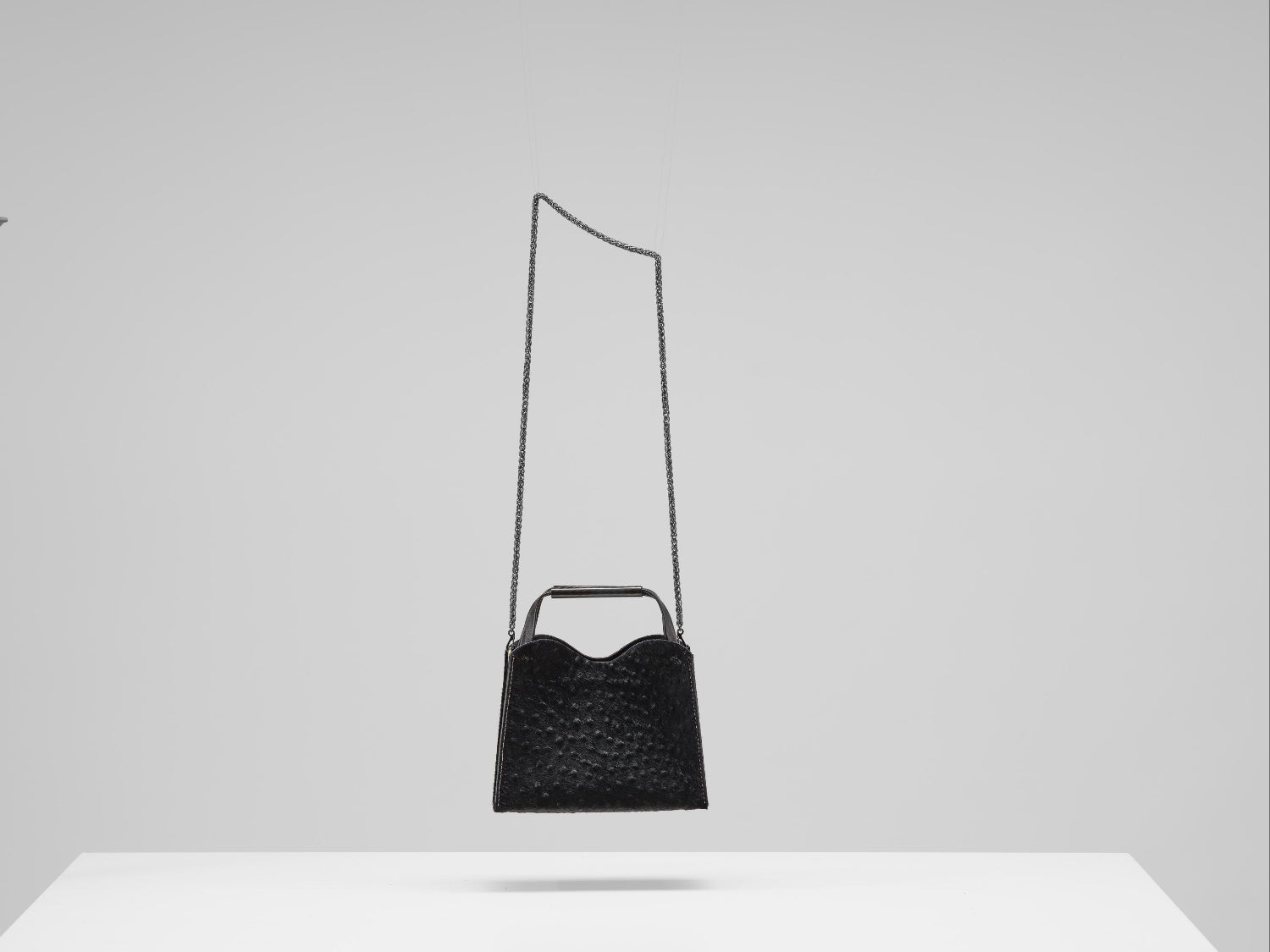 Black handbag with a long strap on a white surface and light gray background