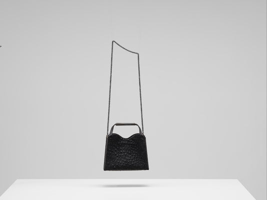 Black handbag with a long strap on a white surface and light gray background